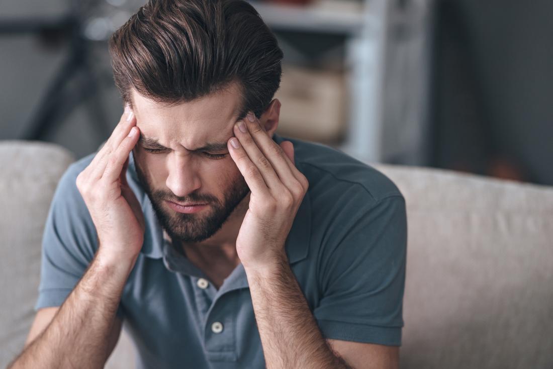 man with migraine headache massaging his temples and frowning
